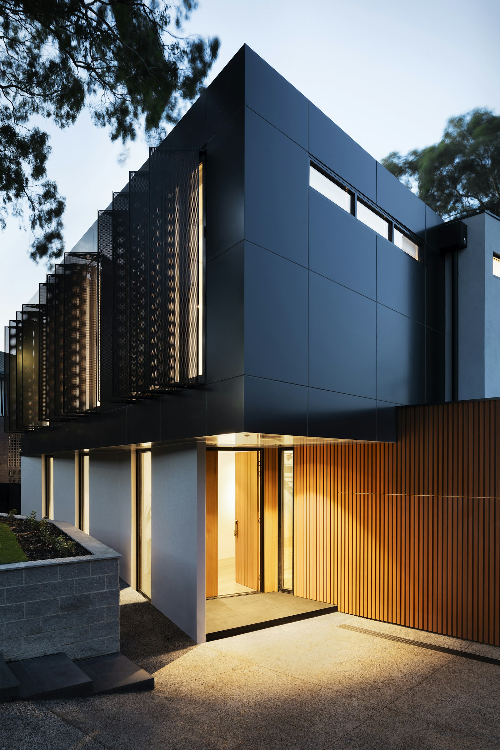Modern house with dark cladding, warm timber screens, and a lit entry
