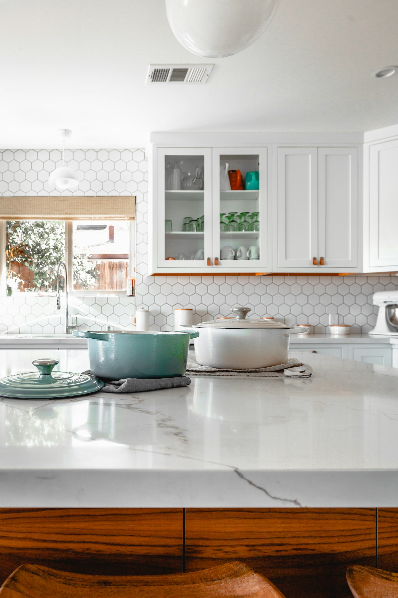 Bright kitchen with a marble island, white cabinets, and a window over the sink